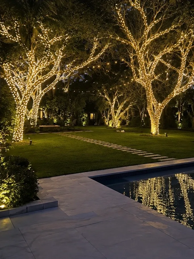 Poolside garden with trees wrapped in warm white Christmas lights reflected in the pool.